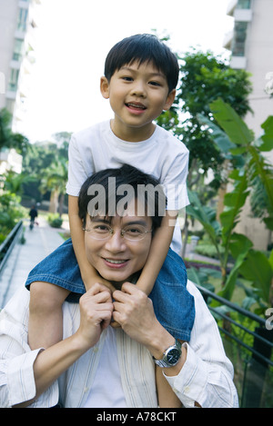 Boy riding on father's shoulders, front view, smiling at camera Stock Photo