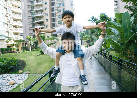 Boy riding on father's shoulders, front view, smiling at camera Stock Photo