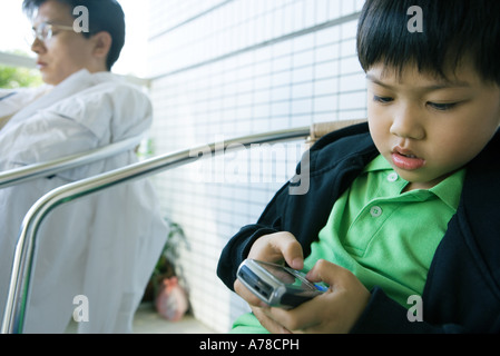 Boy using cell phone while father sits with eyes closed Stock Photo