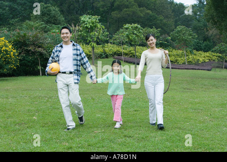 Girl walking hand in hand with parents, full length Stock Photo