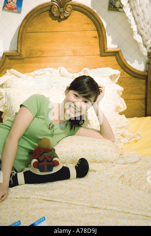 Young woman reclining on bed, smiling at camera Stock Photo