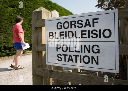 Woman voter with polling card walking to polling station past bilingual dual language Welsh English sign Wales UK Stock Photo