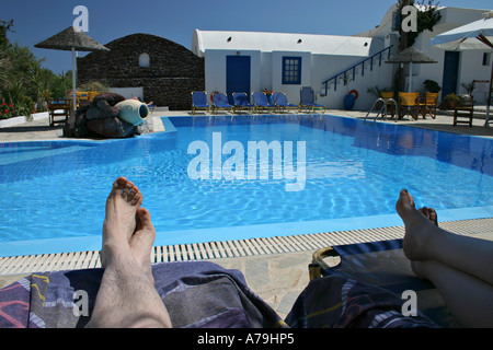 The legs of two people, a couple resting on beach chairs near a blue swimming pool Acrotiri Santorini Greece Stock Photo