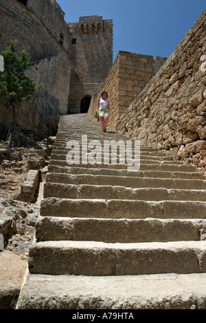 Lindos Acropolis Stairway: A young woman walks down the long stairway that leads up to the fortifications castle surrounding Stock Photo