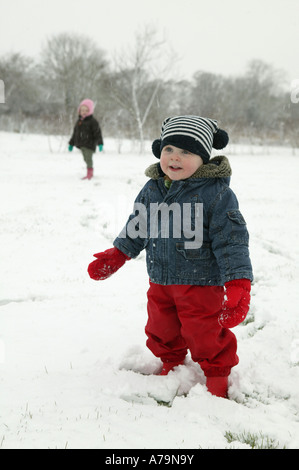 small child in red trousers playing in winter snow landscape Also wearing a blue and white stripy hat Sweet innocent image Stock Photo