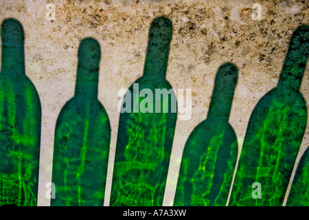 Five green glass bottles arranged closely together cast vibrant shadows on a textured surface Stock Photo