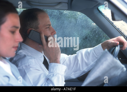 businessman talking on cell phone while driving car in rain while wife reads newspaper Stock Photo