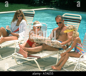 family of four relaxing and reading comics by swimming pool Stock Photo