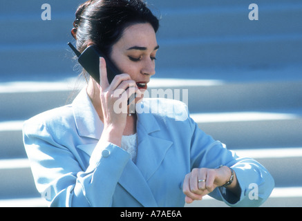 woman executive checking watch while talking on a cell phone on steps of an office building Stock Photo