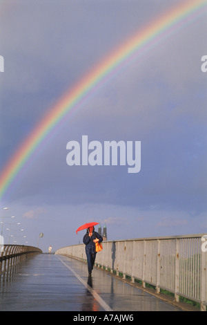 Woman with red umbrella walking over Vasterbro under rainbow in Stockholm Stock Photo