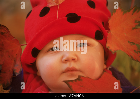 Baby with red wool hat amid fallen autumn leaves Stock Photo
