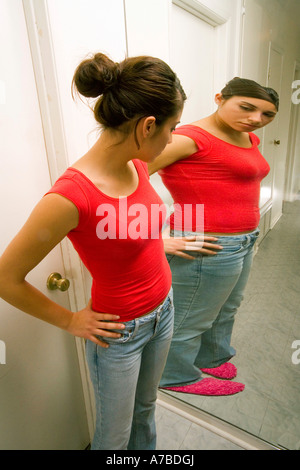 Hispanic teen girl sees herself as overweight in reflection in mirror Model released Stock Photo
