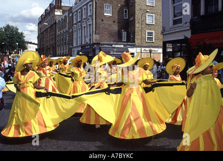 Adult young ladies dressed in yellow orange hopped striped costumes wide brimmed hats sunny street scene London 1992 Notting Hill Carnival Parade UK Stock Photo