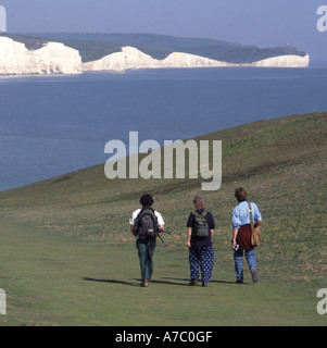Seaford Head walkers on grass downs with Seven Sisters white chalk cliffs beyond Stock Photo