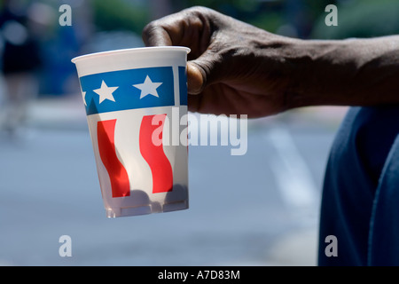 Hand of beggar, panhandler, holding out paper cup with US flag decor on Pennsylvania Avenue, Washington DC. Stock Photo
