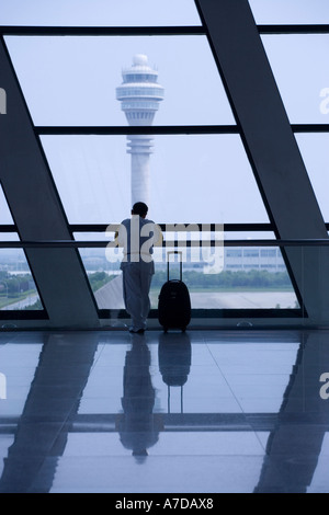 Asia China Shanghai Silhouette of passengers looking out window inside arrivals terminal of Pudong International Airport Stock Photo