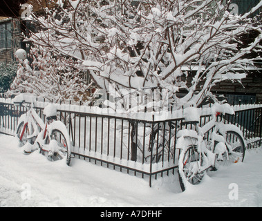 Bicycles leaning against a fence and covered in deep fresh snow after being left out in a snowstorm in Montreal Quebec Canada Stock Photo