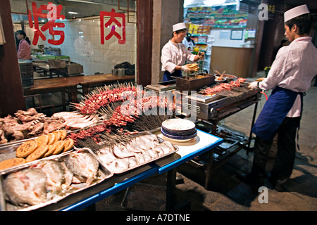 CHINA XI'AN Restaurant workers with variety of ingredients including kabobs fish meat and bread displayed for grilling outside Stock Photo