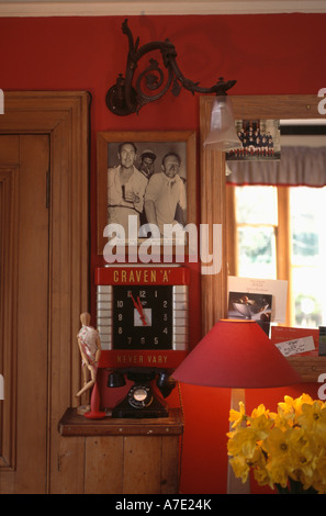 Black+white photograph and Craven A clock on wall in red living room with  collection of cricket memorabilia Stock Photo
