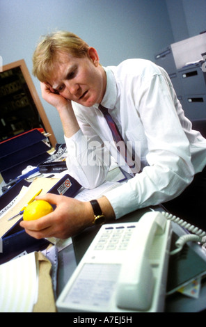 Stressed looking businessman in his office holding an orange Stock Photo