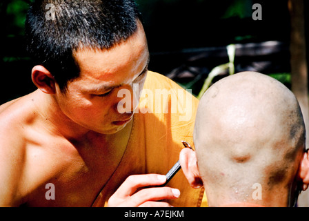 A young Buddhist novice monk shaves the head of another novice monk Stock Photo