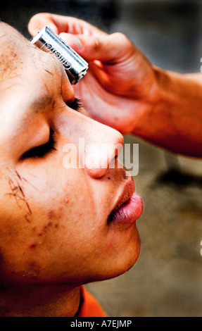 A young Buddhist novice monk shaves the haed of another novice monk Stock Photo