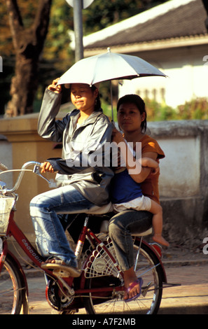 Cyclist shielding sun with umbrella carrying passengers on back of bicycle, Luang Prabang, Laos Stock Photo