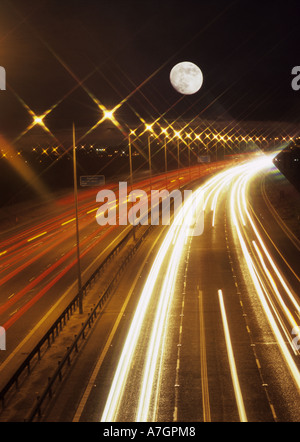 long time exposure of traffic travelling on the m62 motorway at night with the  moon rising  above leeds uk Stock Photo