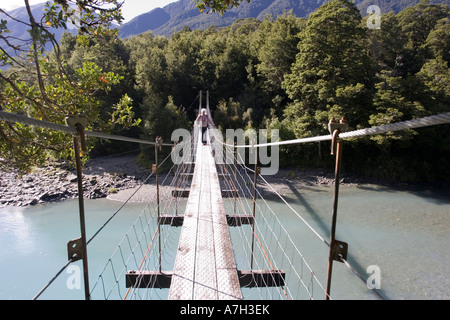 Woman tourist crossing wire suspension bridge over Haast River at Blue Pools at Gates of Haast South Island New Zealand Stock Photo