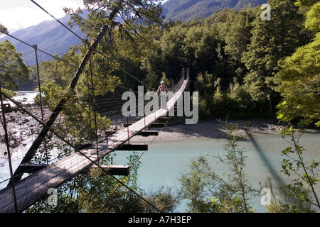 Woman tourist crossing wire suspension bridge over Haast River at Blue Pools at Gates of Haast South Island New Zealand Stock Photo