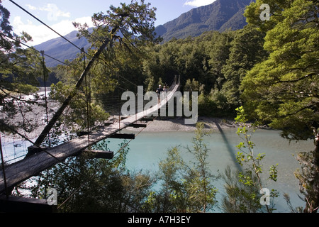 Tourists crossing wire suspension bridge over Haast River at Blue Pools at Gates of Haast South Island New Zealand Stock Photo