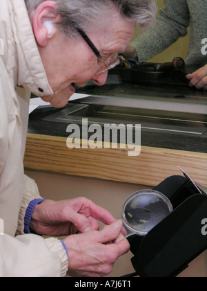 elderly woman using magnifying glass making it easier to see the post office device (collecting pension, withdrawing monies) Stock Photo