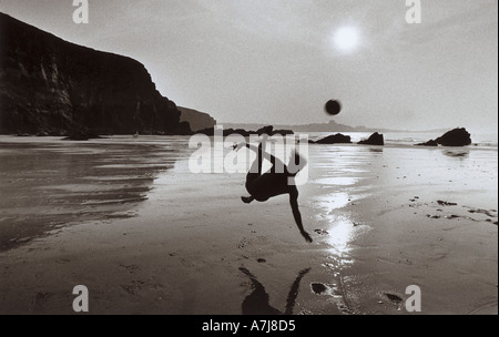 A boy plays a last game of beach football at sunset on Lusty Glaze beach Newquay Cornwall Stock Photo