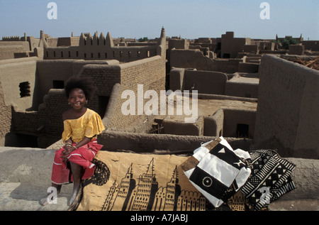 Girl sitting on a traditional flat mud rooftop selling traditional mud cloth paintings or bogolan, Djenné, Mali Stock Photo