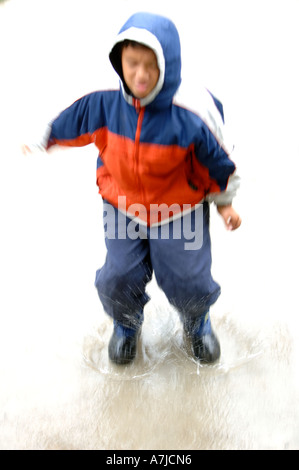 Boy (8-10) playing during bad weather and rain in puddle of water Facial expression Stock Photo