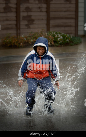 Boy (8-10) playing during bad weather and rain in puddle of water Facial expression Stock Photo