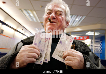 A happy punter with a big cigar waves his wad of winnings in twenty pound notes in a William Hill Betting Shop Stock Photo