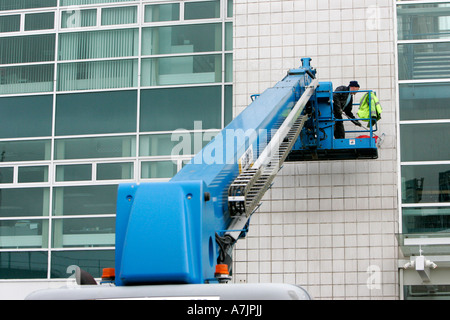 rear view of elevator and worker on elevator platform lift brushing outside wall of office building with white tiles belfast Stock Photo
