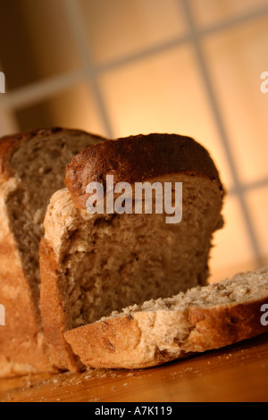 PORTRAIT SHOT OF A LOAF OF BROWN UNCUT BREAD WITH TWO SLICES FALLING OVER AT FRONT WITH A WINDOW IN THE BACKGROUND Stock Photo