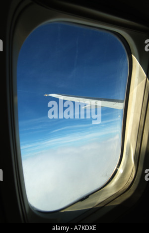View of part of the wing tip seen out of passenger jet aircraft window flying above dense cloud cover airborne over Europe Stock Photo
