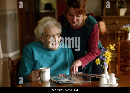 An elderly lady reads a magazine whilst talking to her carer in a old people care home. Stock Photo
