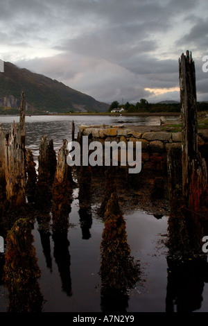 Rotting wooden jetty posts at the end of a stone built victorian pier with overcast threatening stormy sky Loch Etive Scotland