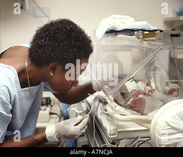 neo-natal unit in hospital with nurse attending to a baby in incubator Stock Photo