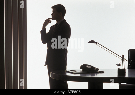 Contemplative male executive standing next to desk Stock Photo