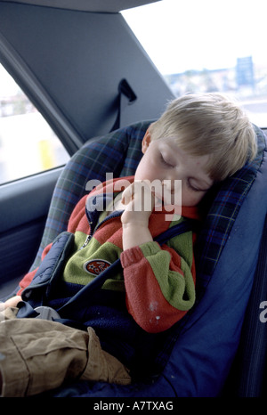 three year old boy belted into his safety seat sleeping in the back of a car Stock Photo