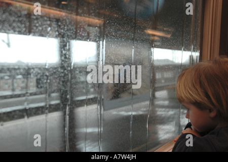 boy in front of window pane wet from rain in a railway building, Germany, Hesse, Frankfurt am Main Stock Photo