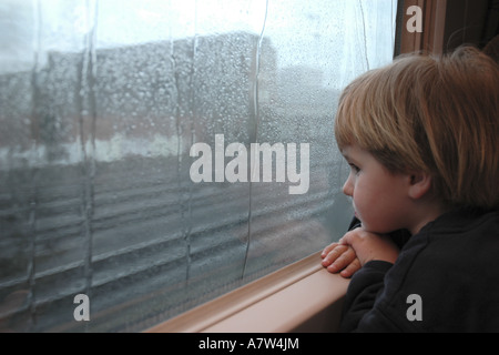 boy in front of window pane wet from rain in a railway building, Germany, Hesse, Frankfurt am Main Stock Photo