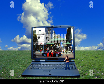 Tiny young woman standing on laptop on wide lawn, looking at city scene Stock Photo