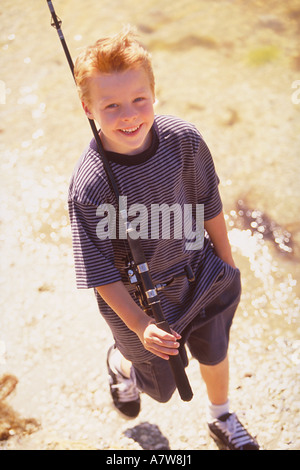 portrait of red-headed 10 year old boy walking with a fishing rod at the  bank of a river Stock Photo - Alamy