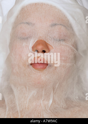 Womans face covered with white mesh for protection from a clay mask Stock Photo